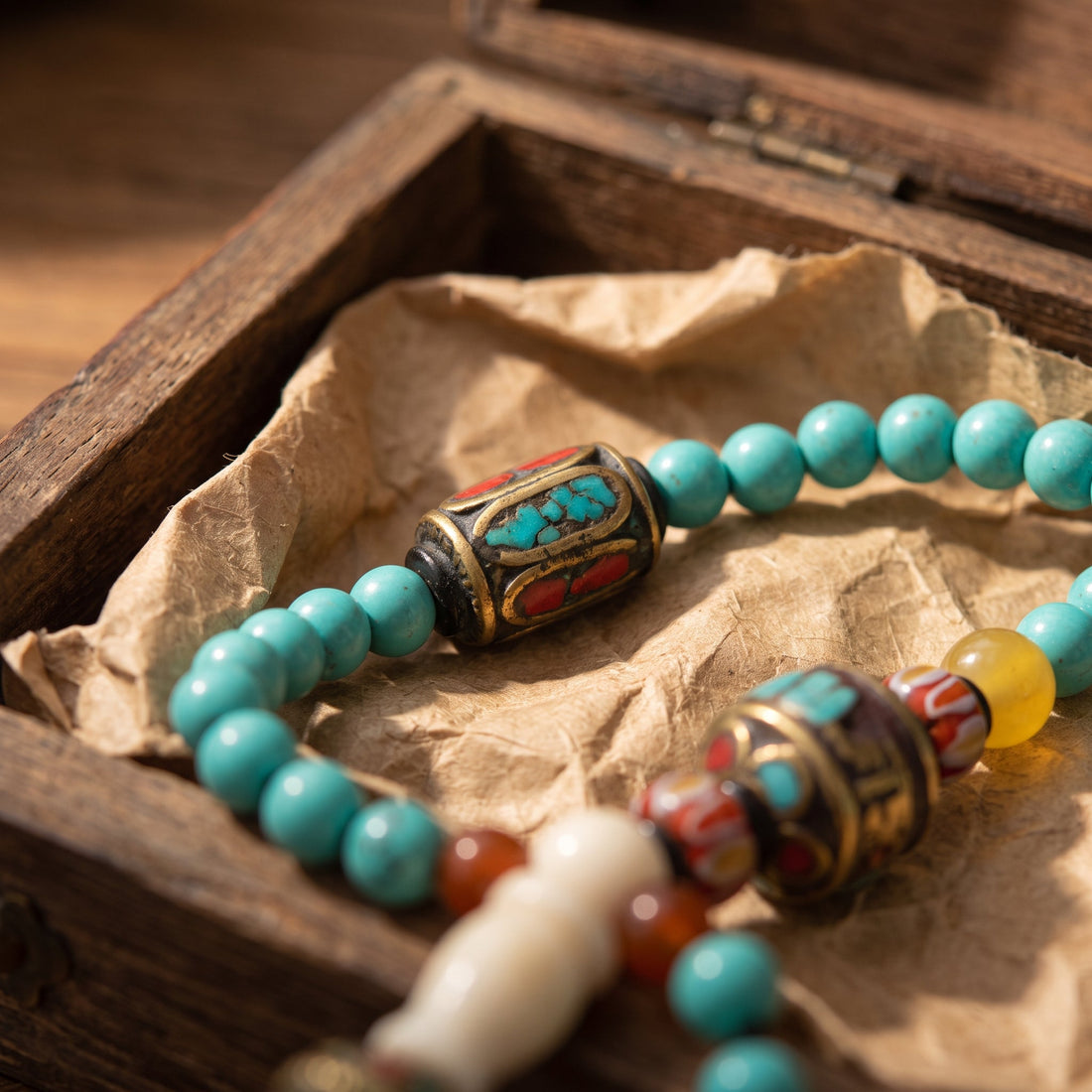Turquoise mala with an inlaid metal bead resting in an old wooden box lined with paper
