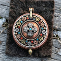 Round copper gau box pendant, front face with a silvery double vajra and stabilized turquoise centre, on dark yak felt with frost
