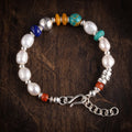 Pearl and mixed bead bracelet lying flat on dark wood: white pearls, a deep blue rondelle, a large hammered 925 sterling silver bead, two honey-orange discs and a blue-green bead, with a silver S-hook and extender chain