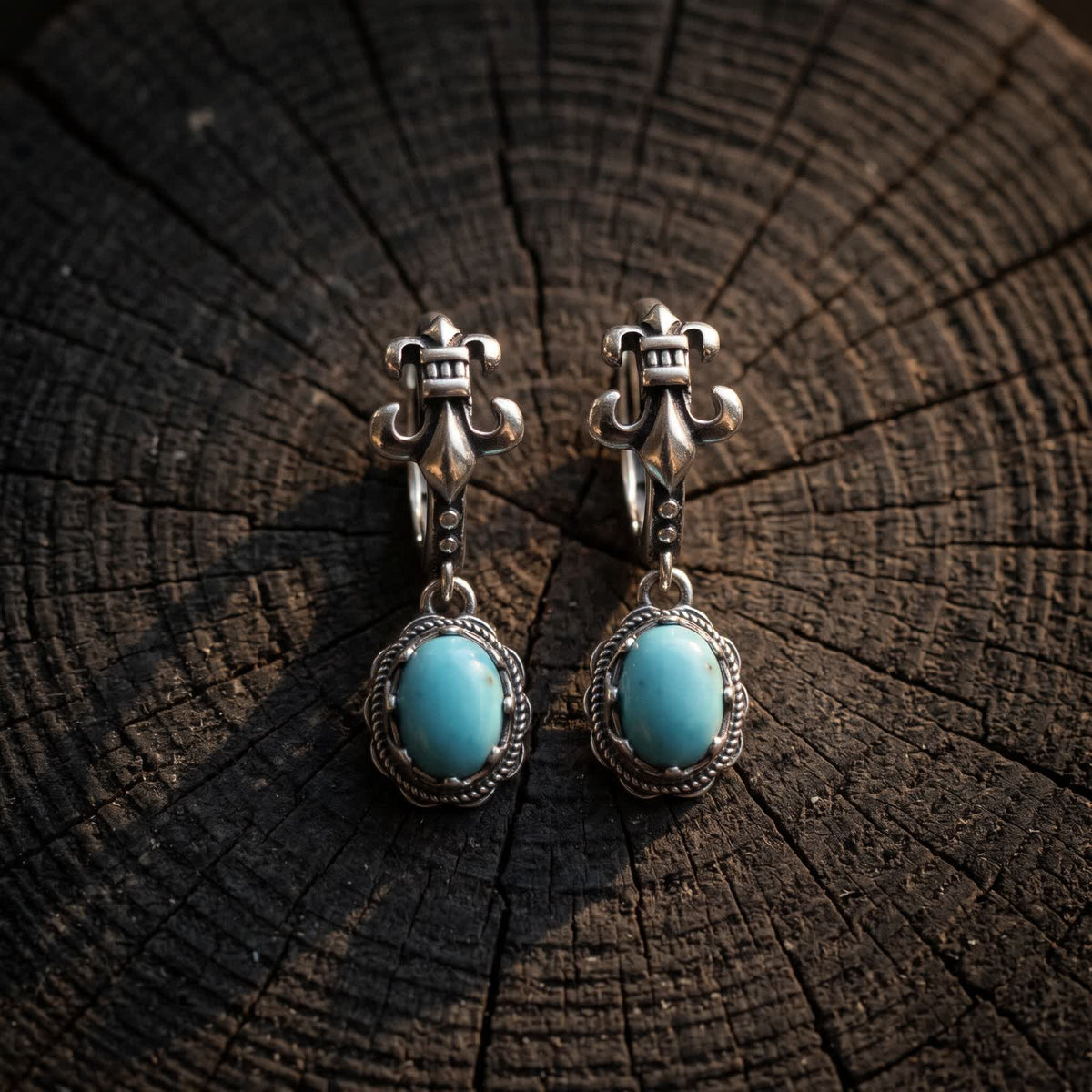 Pair of fleur-de-lis hoop earrings in 925 sterling silver with oval turquoise drops on a dark wooden stump