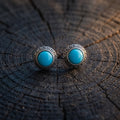 Pair of round turquoise stud earrings with a textured 925 sterling silver bezel on a dark wooden stump in warm side light