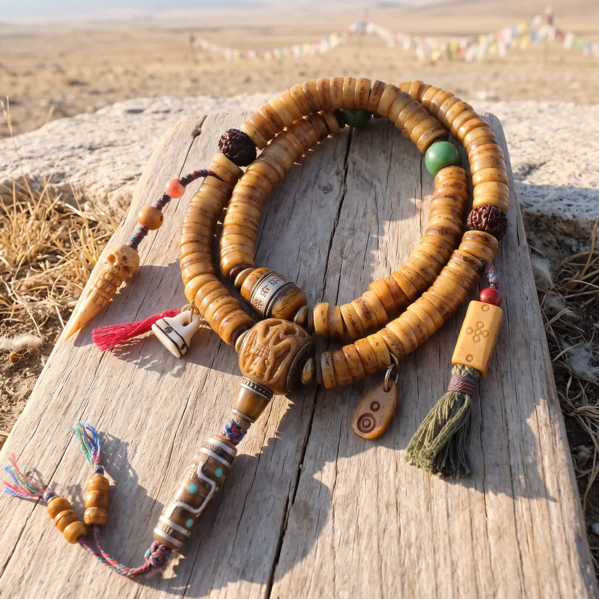 Honey yak bone disc mala coiled on sun-bleached wood in morning light, with carved bone guru bead, bone dzi-pattern bead, two counters and green and red tassels