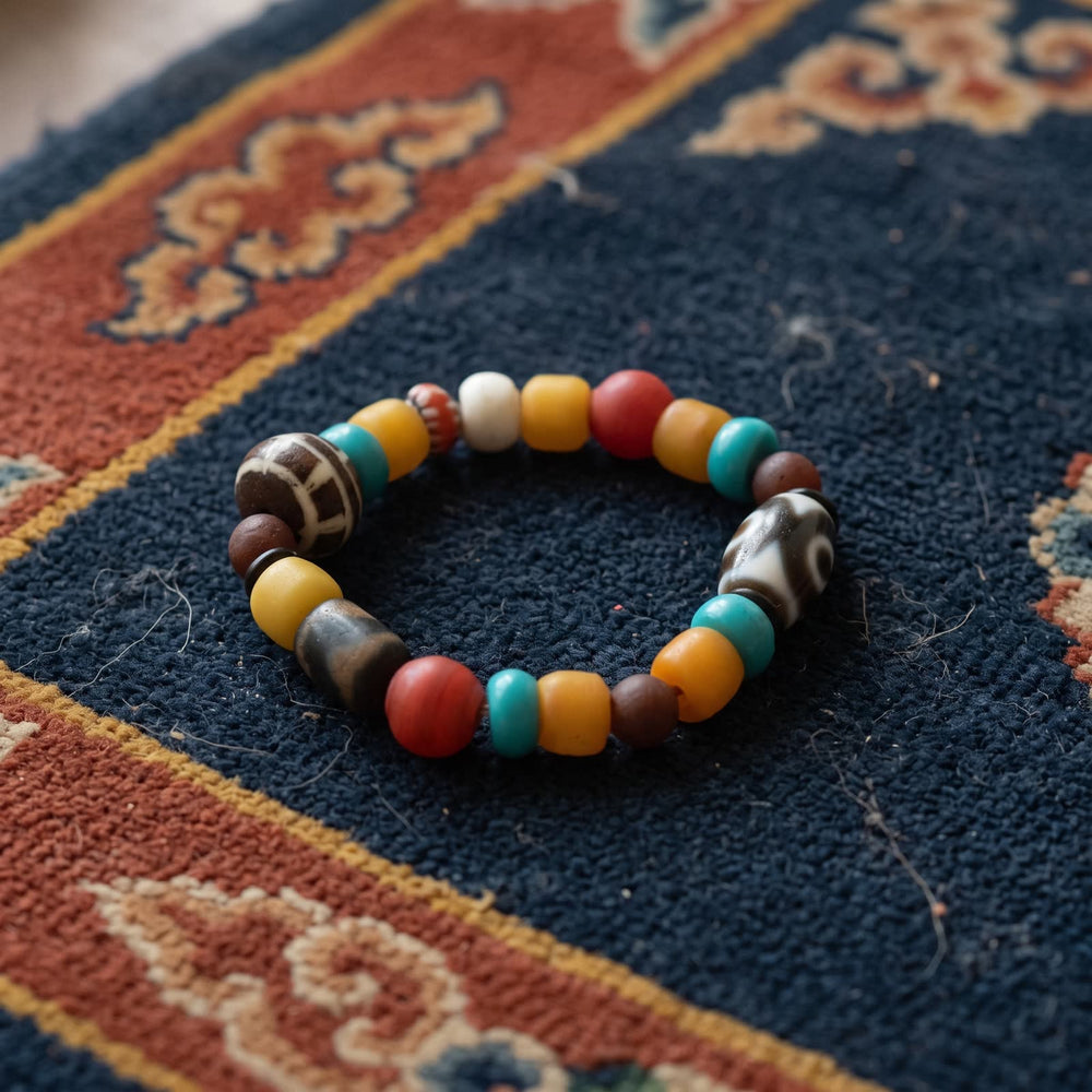 Multi-bead bracelet with an agate dzi, a grid-patterned yak bone bead, yellow ox bone barrels, turquoise and red beads on an indigo khaden rug