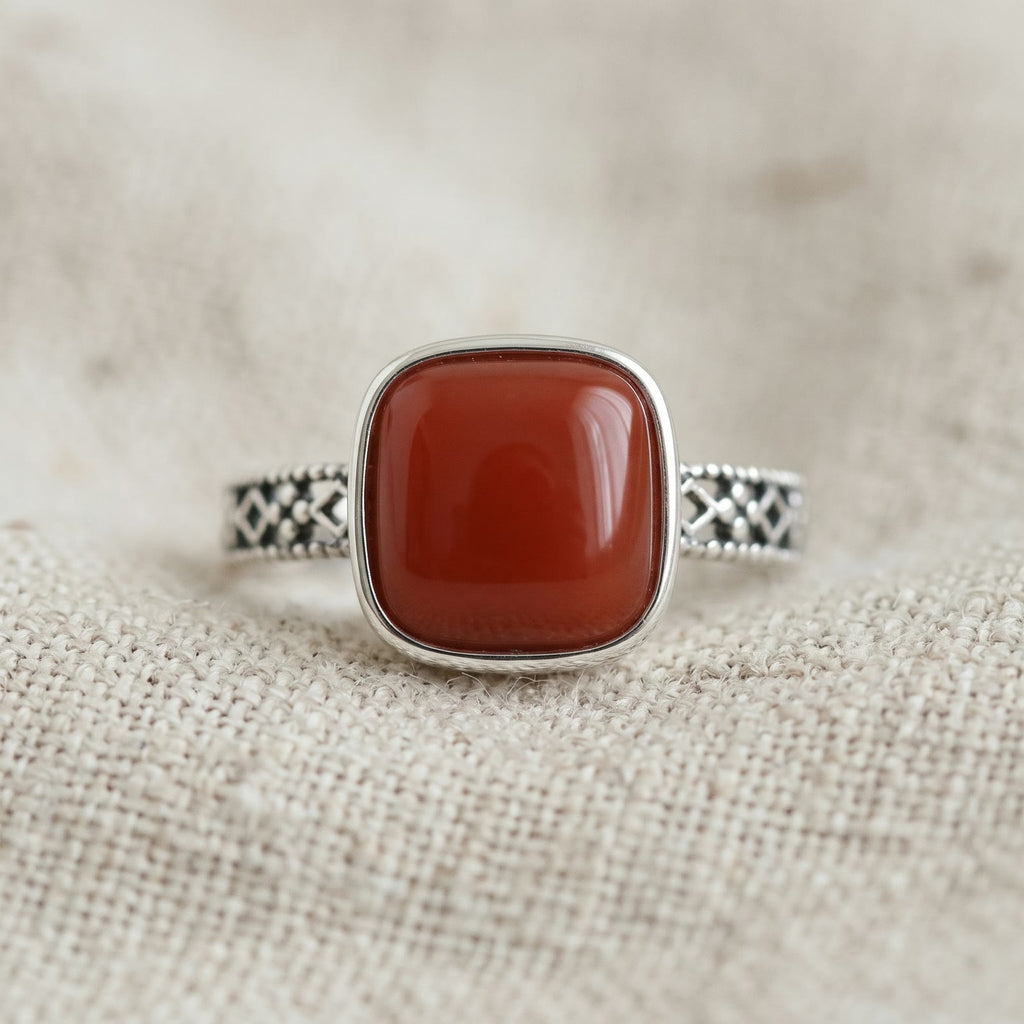 Close-up of an adjustable ring with a square red stone in a smooth bezel and an openwork band, resting on oatmeal linen