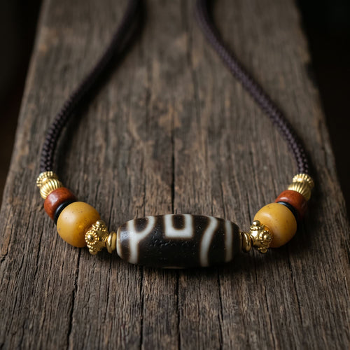 Agate dzi bead choker on a dark brown braided cord, flanked by golden spacers, yellow barrel beads and red beads, resting on a weathered wood plank in soft warm side light