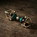 Five-pronged vajra with blue-green inlay cones, lying on an old weathered wood tabletop in soft warm side light