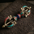 Vajra with red, blue-green and deep blue inlay, lying on dark brown handwoven wool cloth in soft warm side light