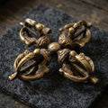 Double vajra lying on charcoal wool felt in soft warm side light, its four heads forming a cross