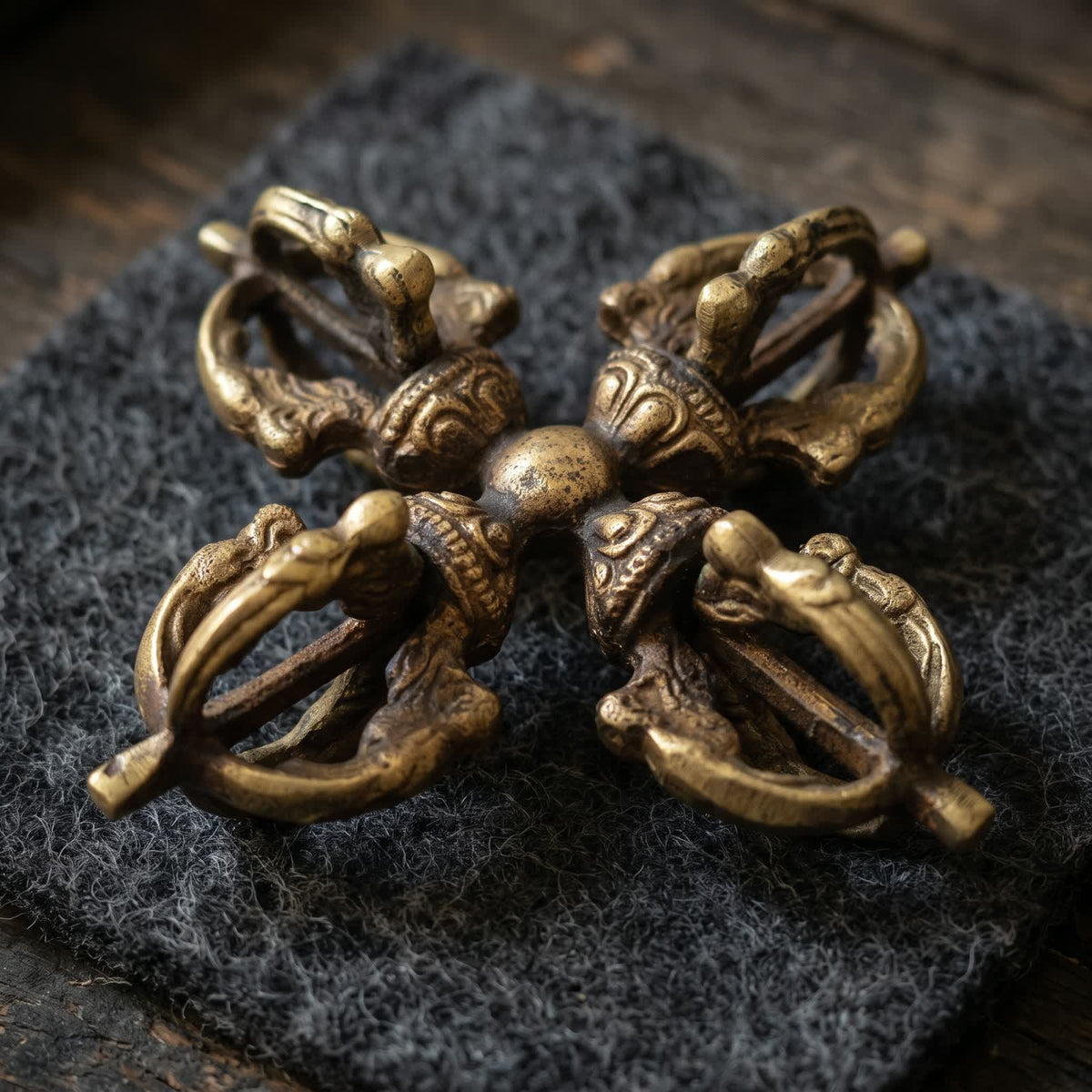 Double vajra lying on charcoal wool felt in soft warm side light, its four heads forming a cross