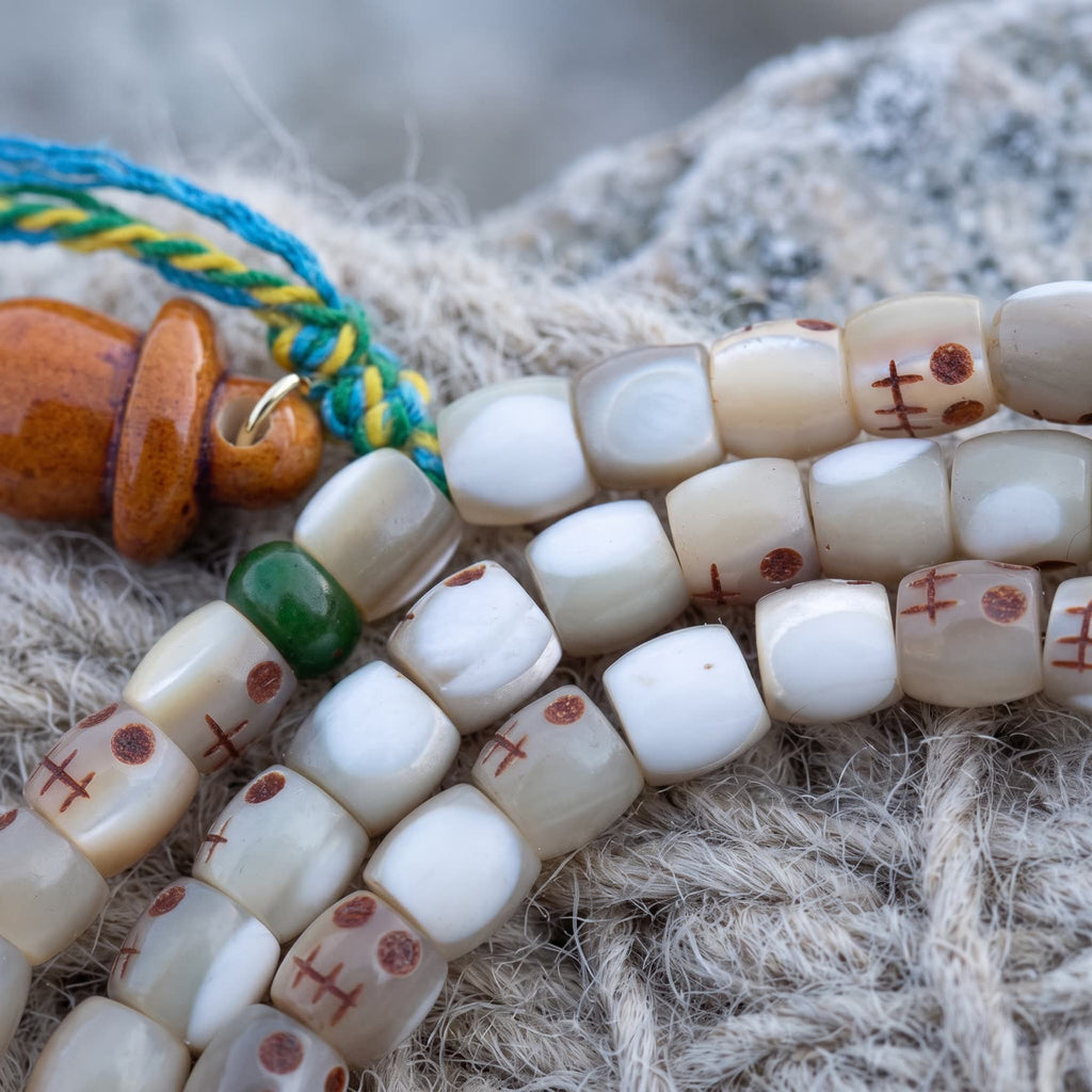 Close-up of milky fish bone beads, some carved with small skull faces with red-brown eyes, beside a green bead and an orange gourd charm