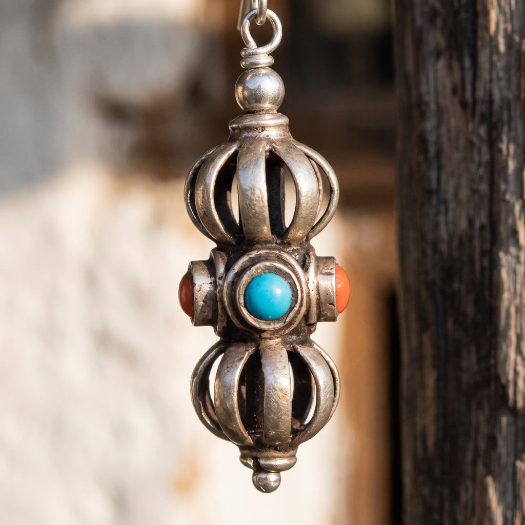 Close-up of one vajra drop earring: open rib cages with a dark core, and a blue stone and red stones on the middle band