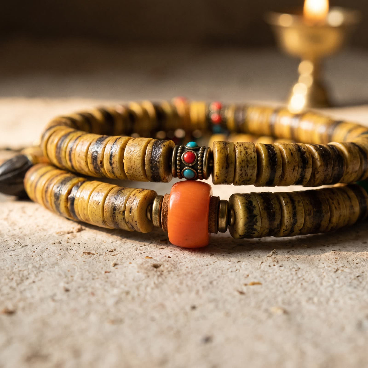Close-up of honey-yellow bone disc beads with dark brown stripes, an orange bead between metal and leather spacers, and a metal bead inlaid with red and blue-green dots