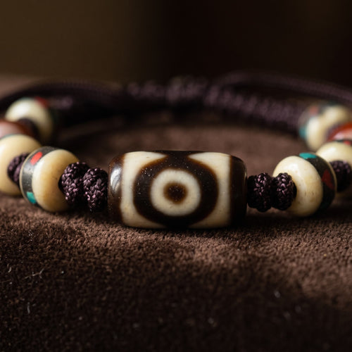 Macro close-up of the agate dzi bead showing its single eye in deep brown and cream, between knotted cord and inlaid disc beads