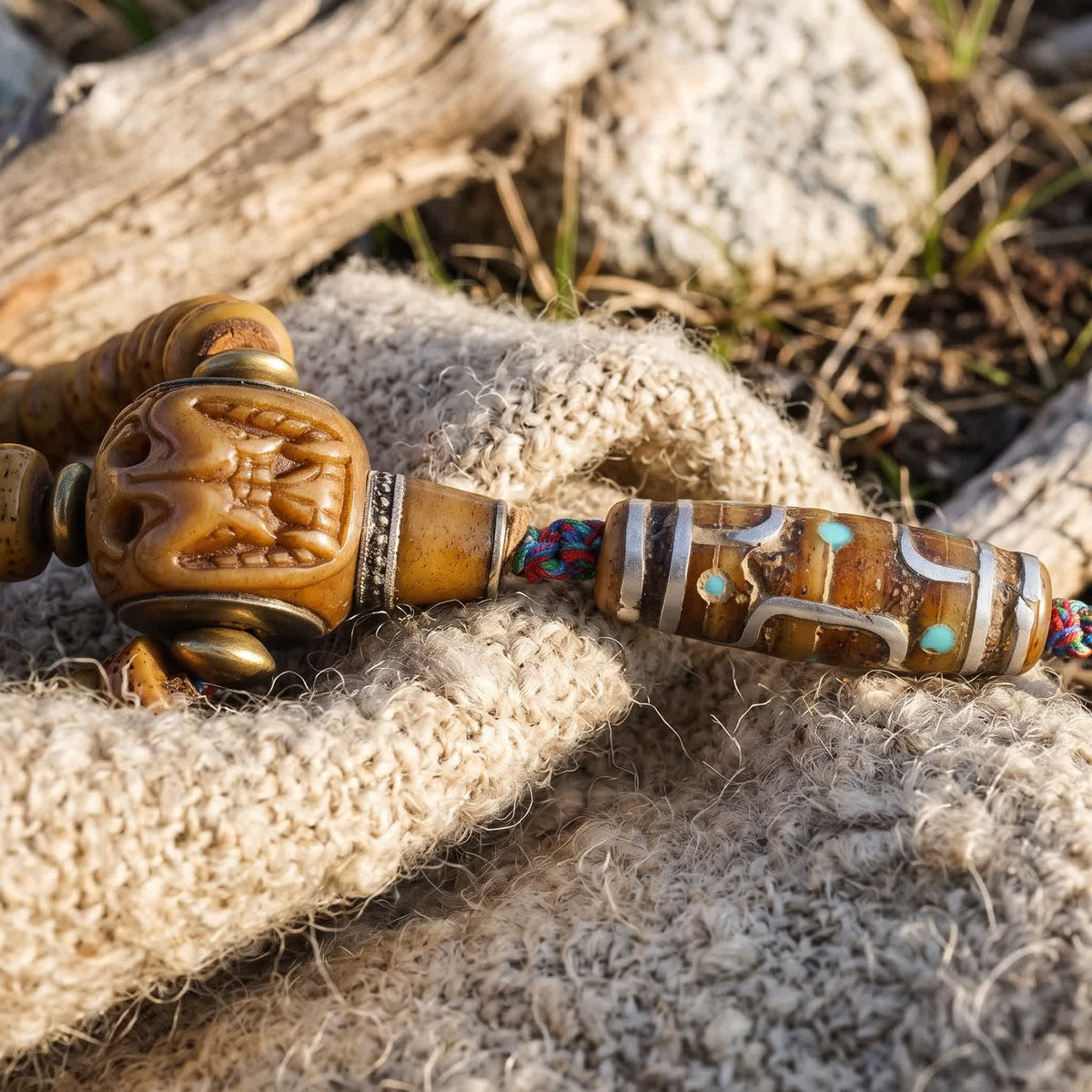 Carved bone guru bead and a bone dzi-pattern bead inlaid with silvery metal lines and blue-green dots, on undyed wool