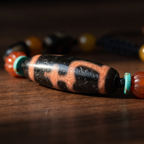 Macro close-up of the large black agate dzi bead with salmon-pink stepped vase-pattern lines and a finely pitted surface