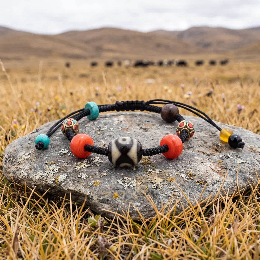 Dalo dzi cord bracelet on a flat lichen-spotted stone in dry plateau grass, a herd of yaks grazing in the distance