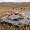 Five-color cord bracelet on a flat stone in dry plateau grass, a few yaks grazing on the hills in the distance