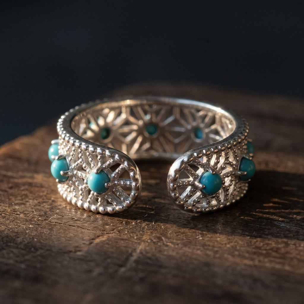 The open ends of the adjustable sterling silver lace ring, each rounded end set with a blue-green stone, the star lattice visible inside the band
