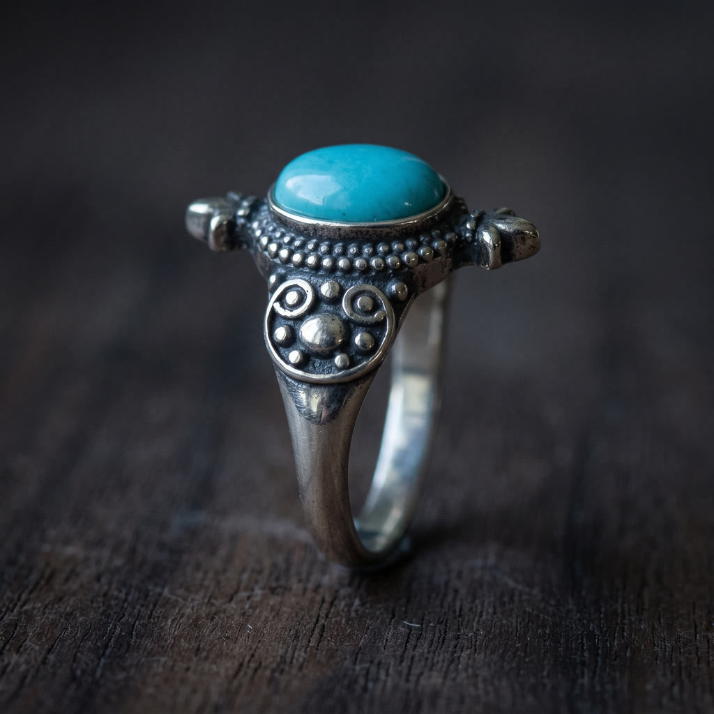 Side view of the oval turquoise ring showing the plain bezel, granulated border, a fleur tip and a scroll-and-dot shoulder plate