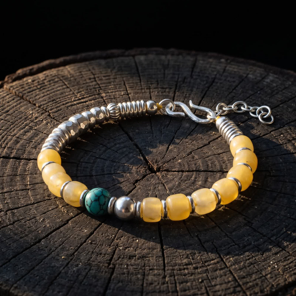 Honey-yellow bead and turquoise bracelet resting on a dark tree stump against a black background in low warm light