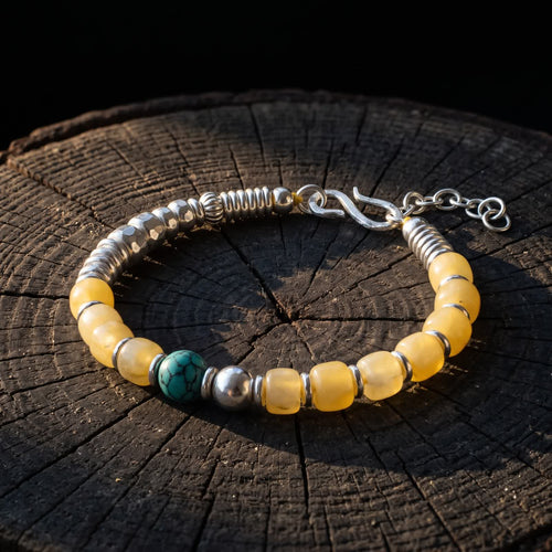 Honey-yellow bead and turquoise bracelet resting on a dark tree stump against a black background in low warm light