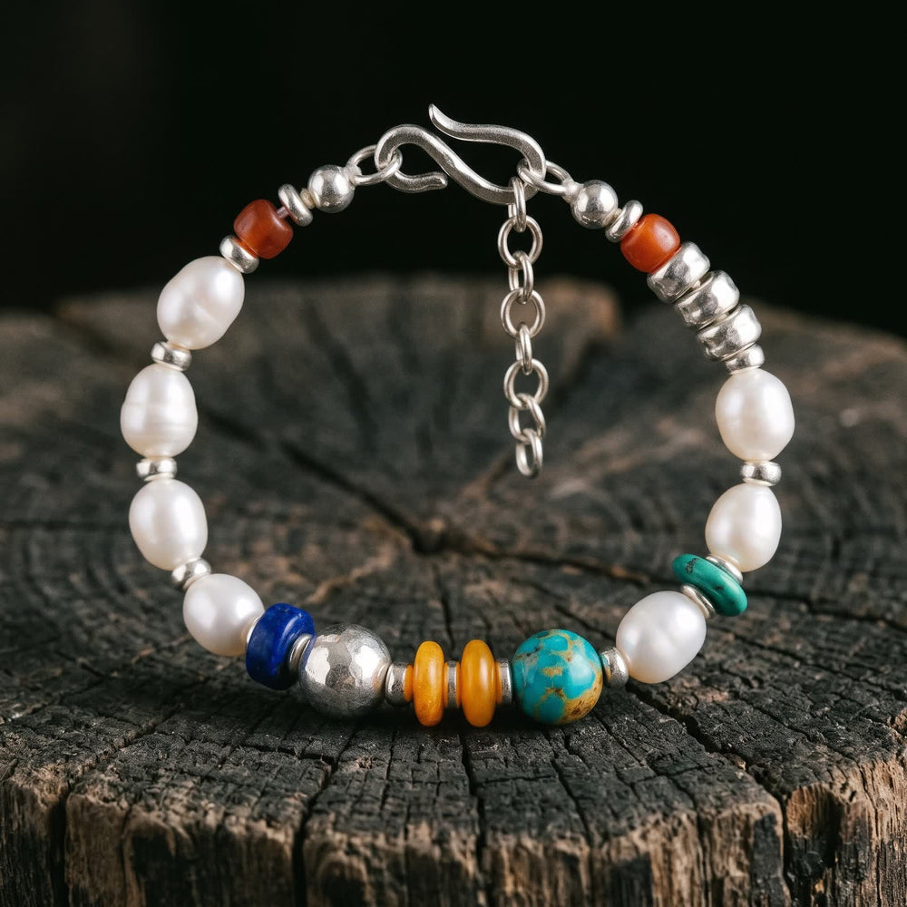 Pearl bracelet standing on a dark tree stump against black, its coloured section of deep blue, hammered silver, honey-orange and blue-green beads facing forward