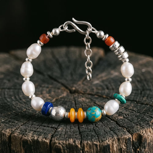 Pearl bracelet standing on a dark tree stump against black, its coloured section of deep blue, hammered silver, honey-orange and blue-green beads facing forward