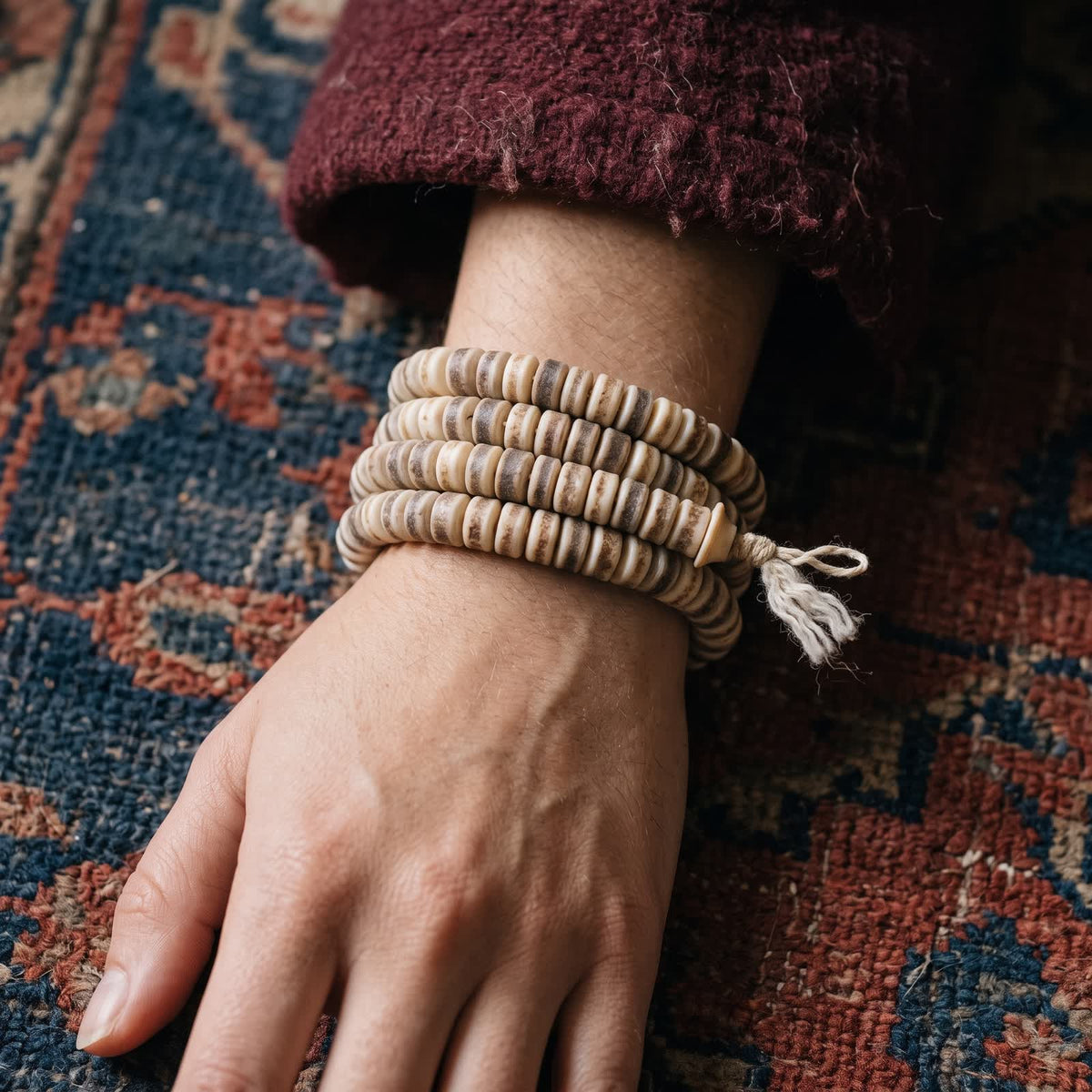 Yak bone barrel bead mala wrapped four times around a woman's wrist below a maroon wool sleeve