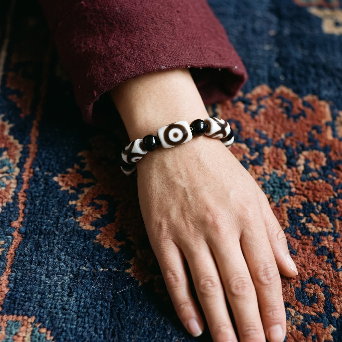 Agate dzi and black agate bead bracelet worn on a woman's wrist below a maroon wool sleeve