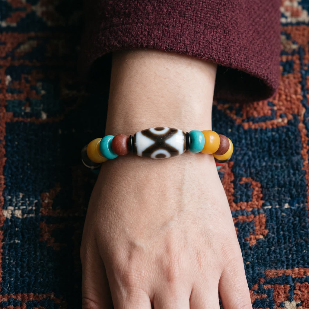 Multi-bead bracelet on a woman's wrist with the agate dzi on top, below a maroon wool sleeve