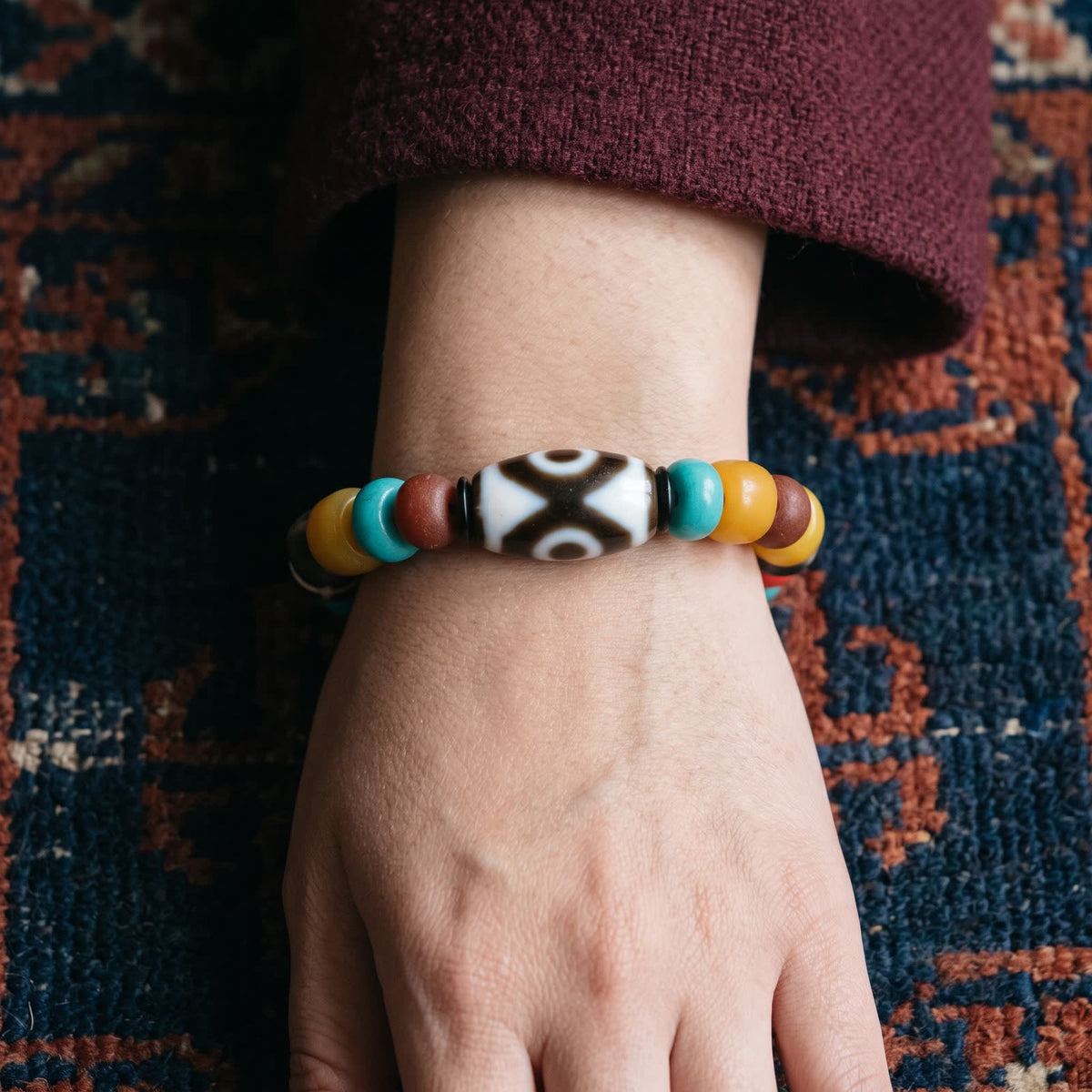 Multi-bead bracelet on a woman's wrist with the agate dzi on top, below a maroon wool sleeve