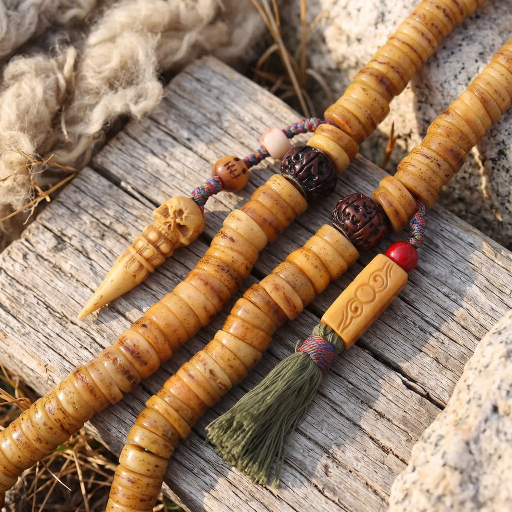Two counters: a carved bone skull and phurba with a pink bead, and a carved bone bar with a red bead and olive-green tassel