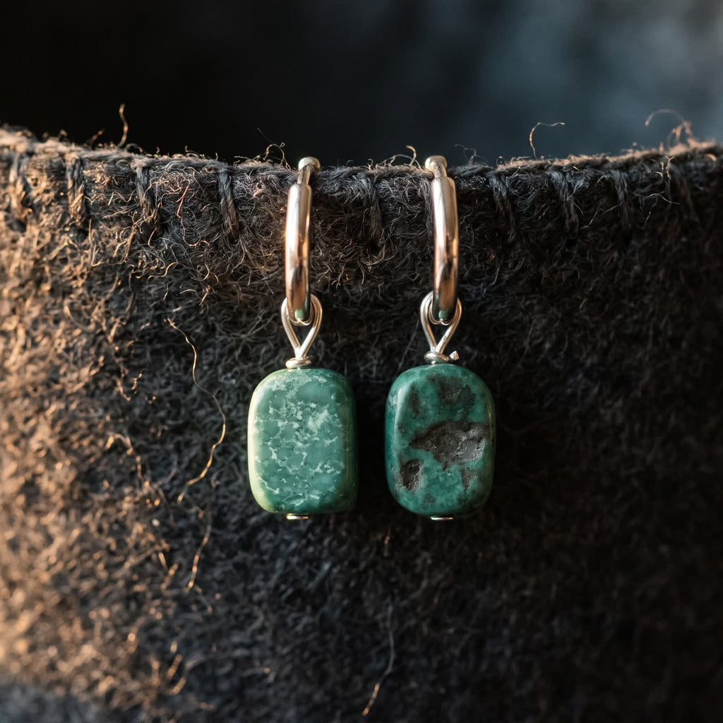 Two hoop earrings with green mottled stone drops hanging from the stitched edge of dark wool felt