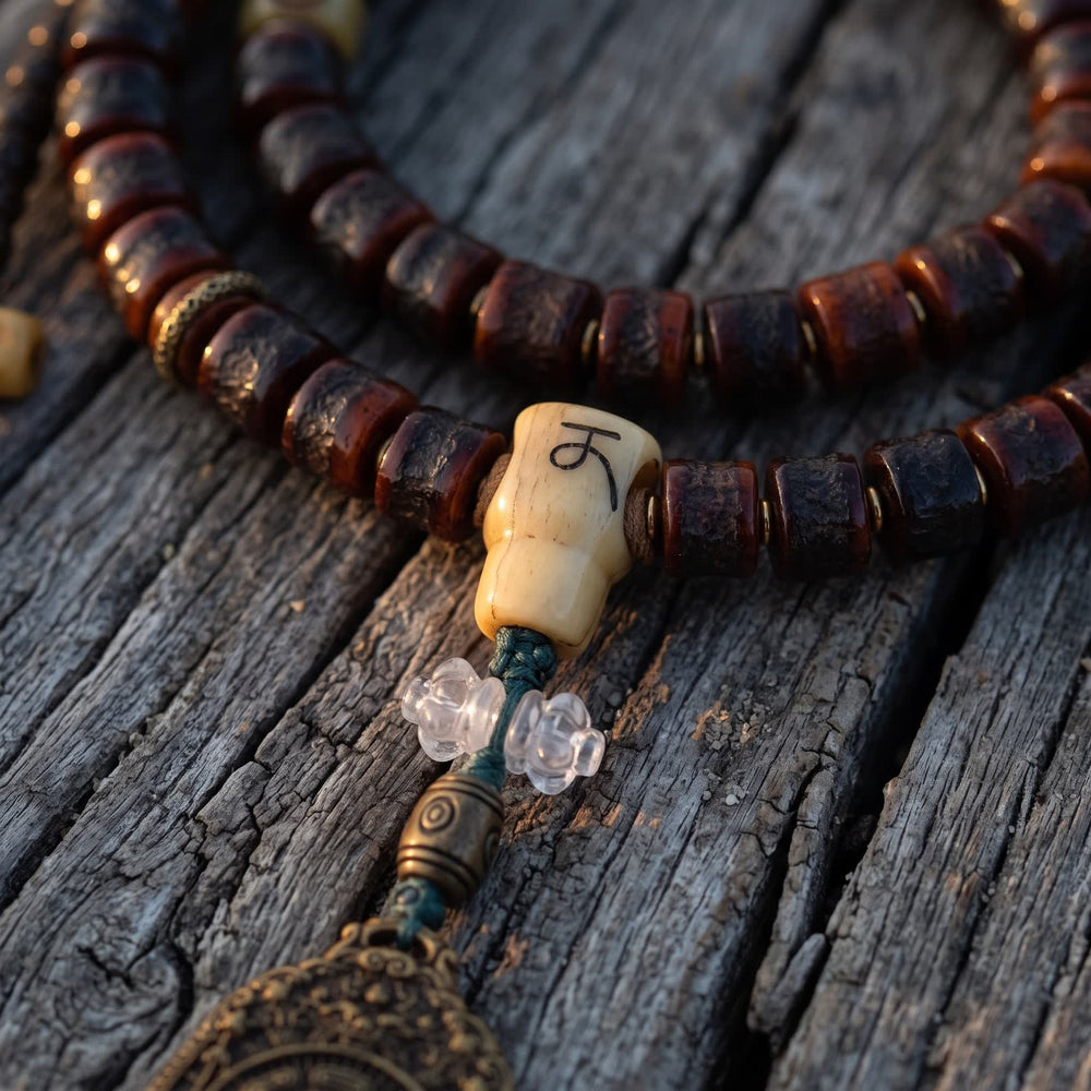 Bone guru bead with an incised letter, two clear flower beads and a metal barrel bead above the pendant, on weathered wood