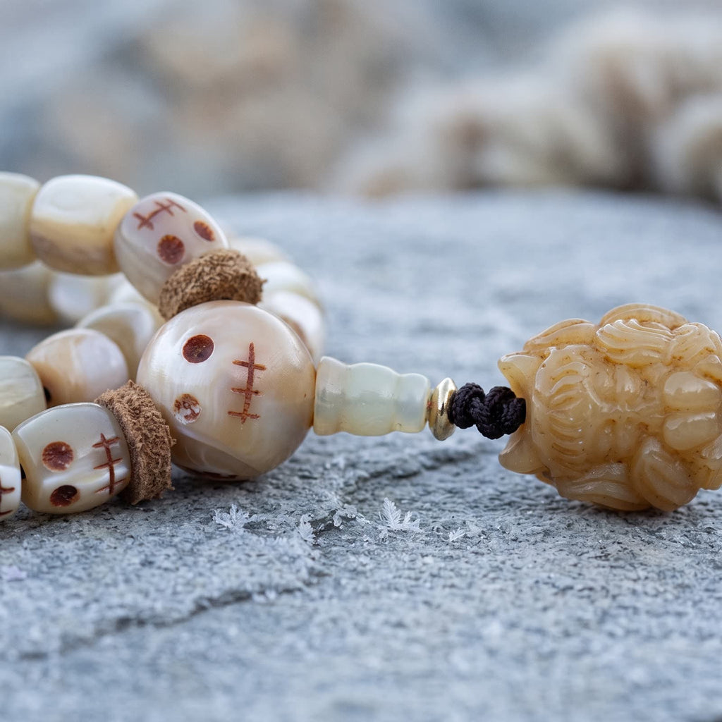 Skull-face guru bead with leather spacers and a translucent stem above a carved bone pendant, on frosted slate