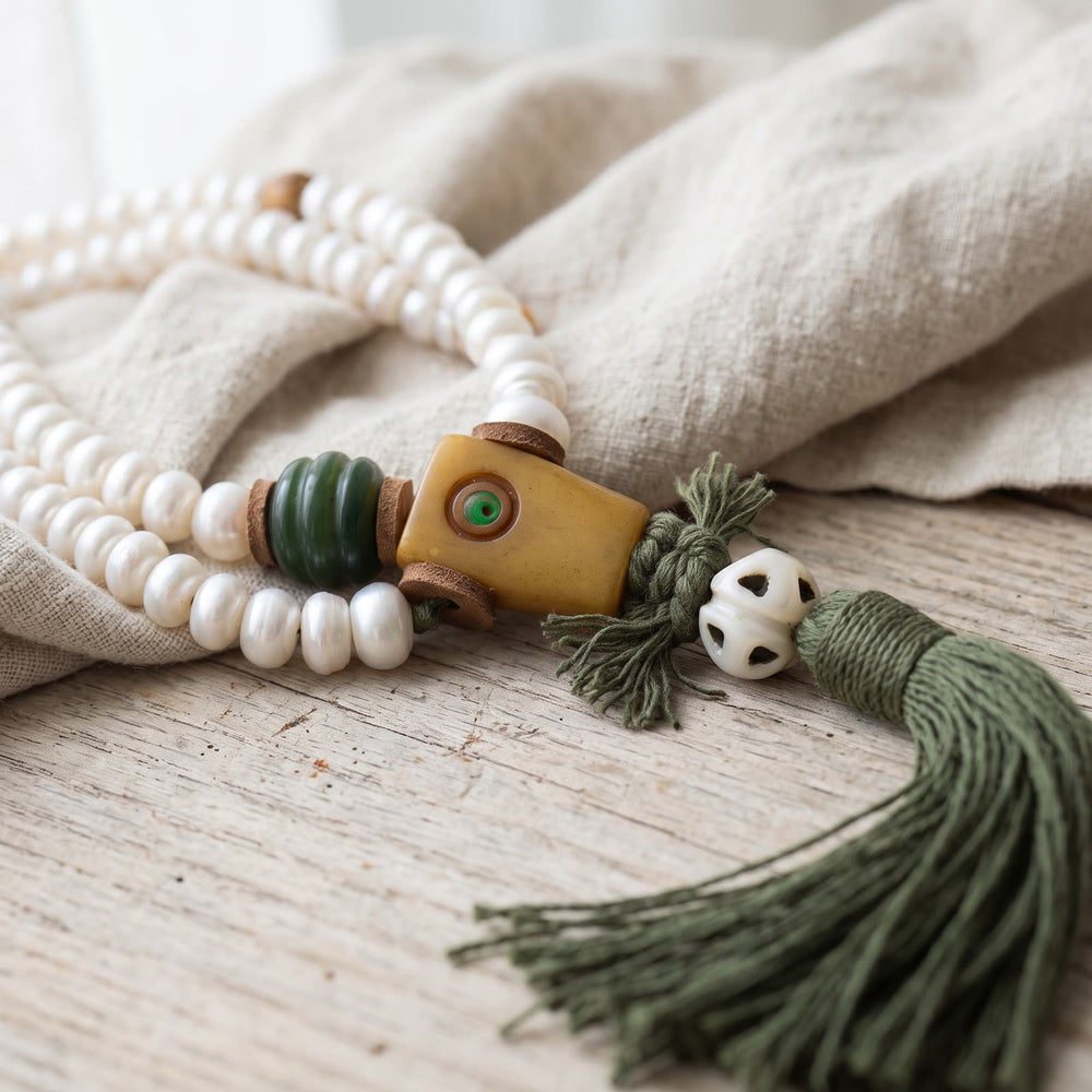 Squared guru bead with a small green inlaid dot, a green ribbed bead and leather spacers, above an openwork white bead and a dark green tassel