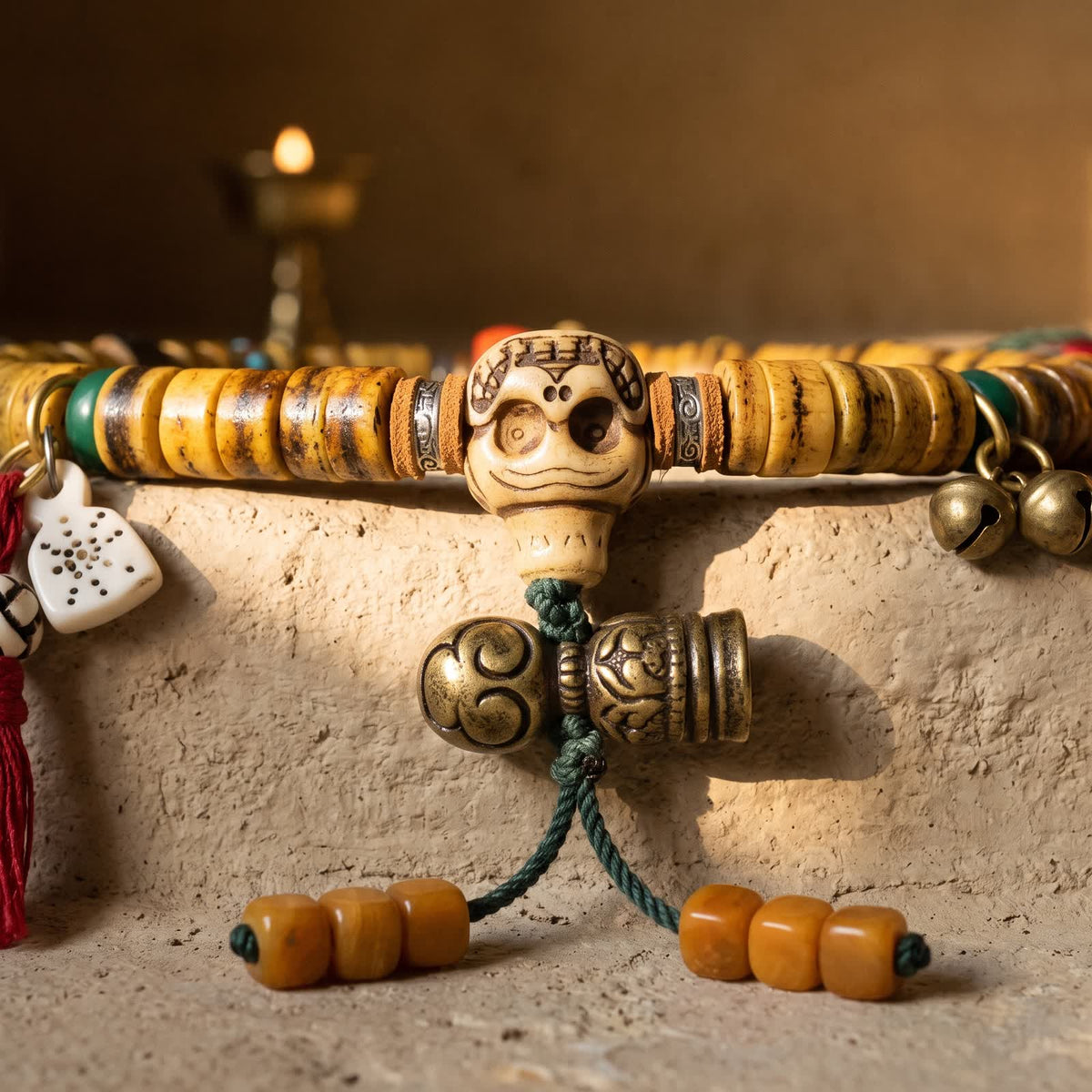 Carved bone skull guru bead with leather spacers, above a golden scroll bead and cylinder on a green cord ending in honey-orange cube beads