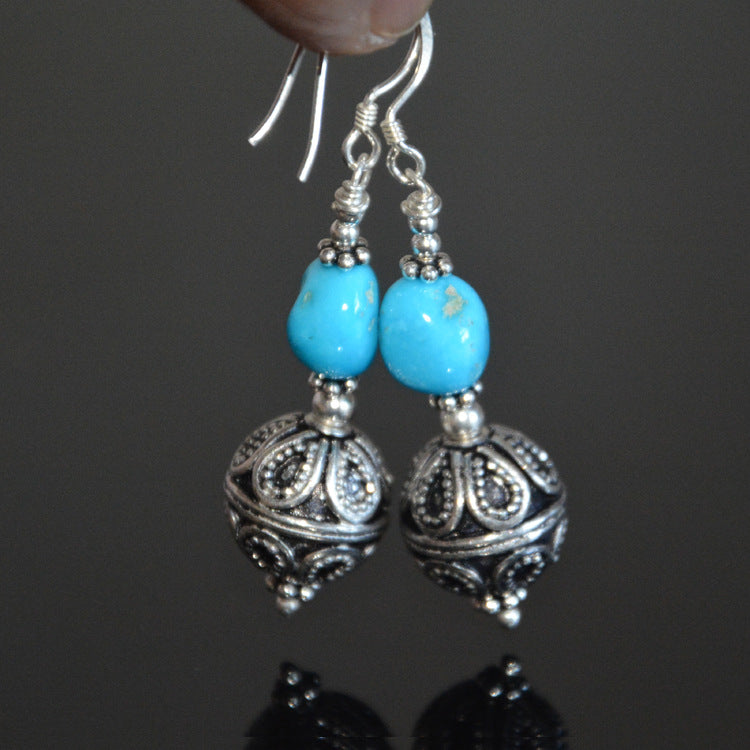 Turquoise and filigree ball drop earrings held by the ear wires, full length