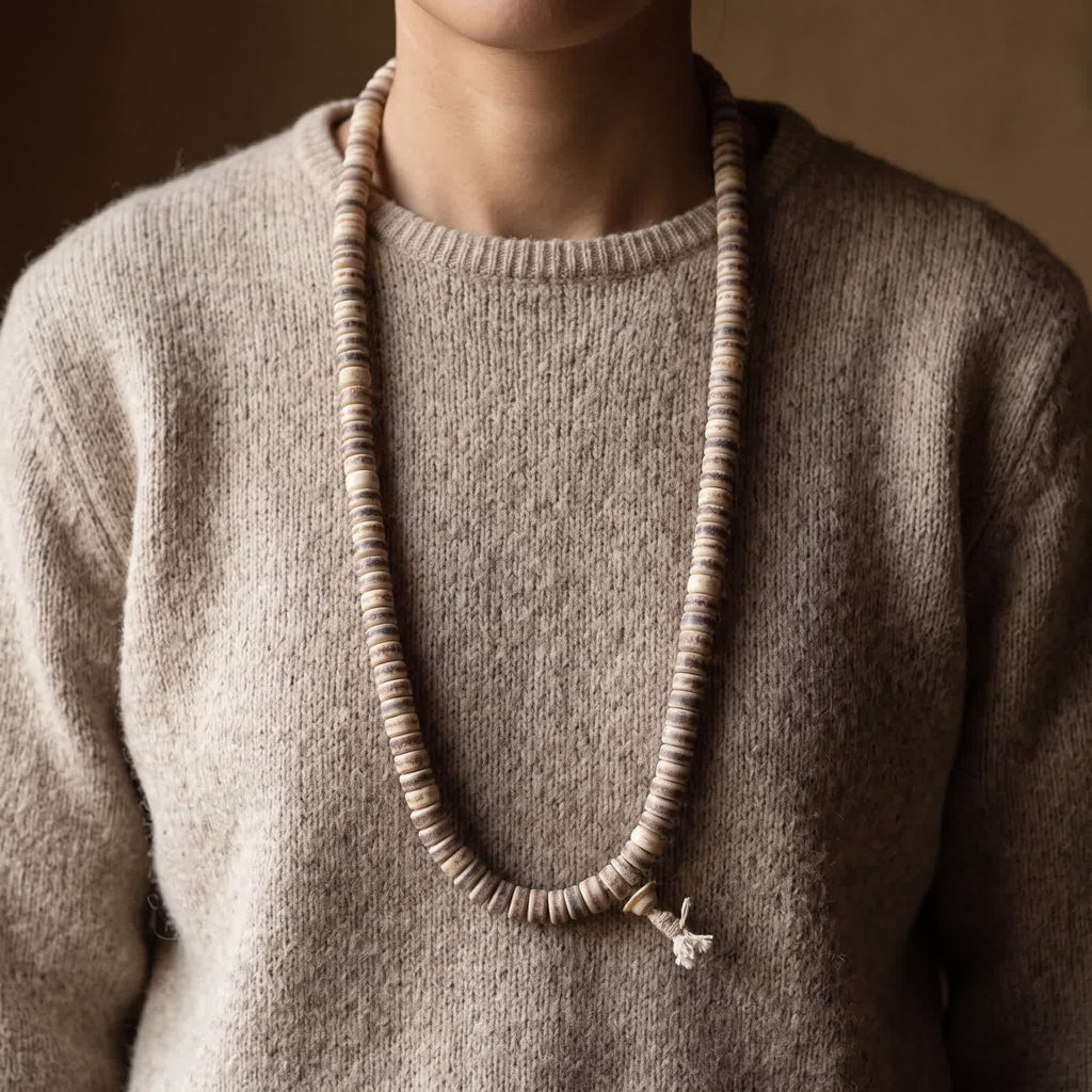 Yak bone barrel bead mala worn as a chest-length necklace over an oatmeal wool sweater