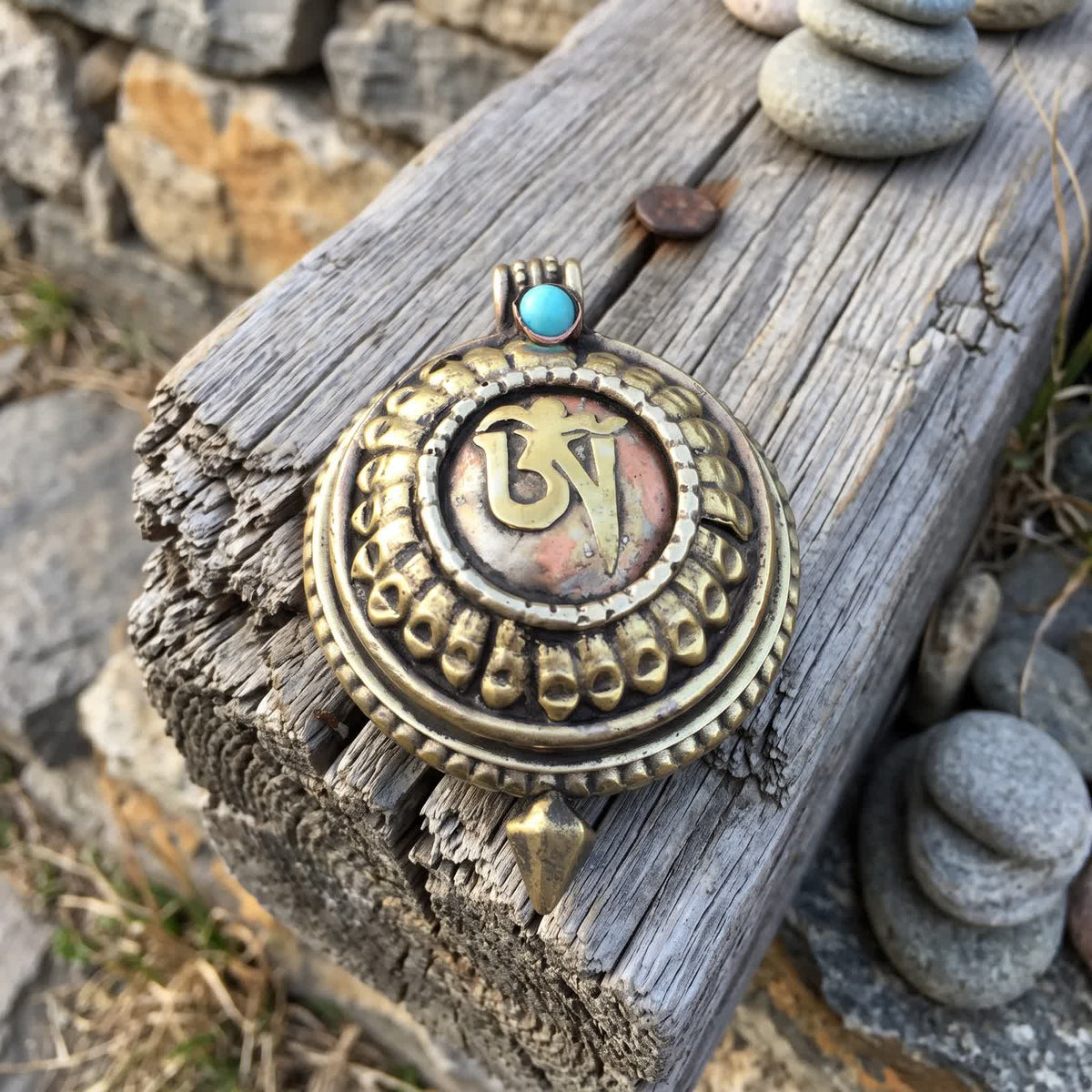 Round golden gau box pendant with a raised Om symbol on a copper-red centre, lying on an old weathered wooden beam