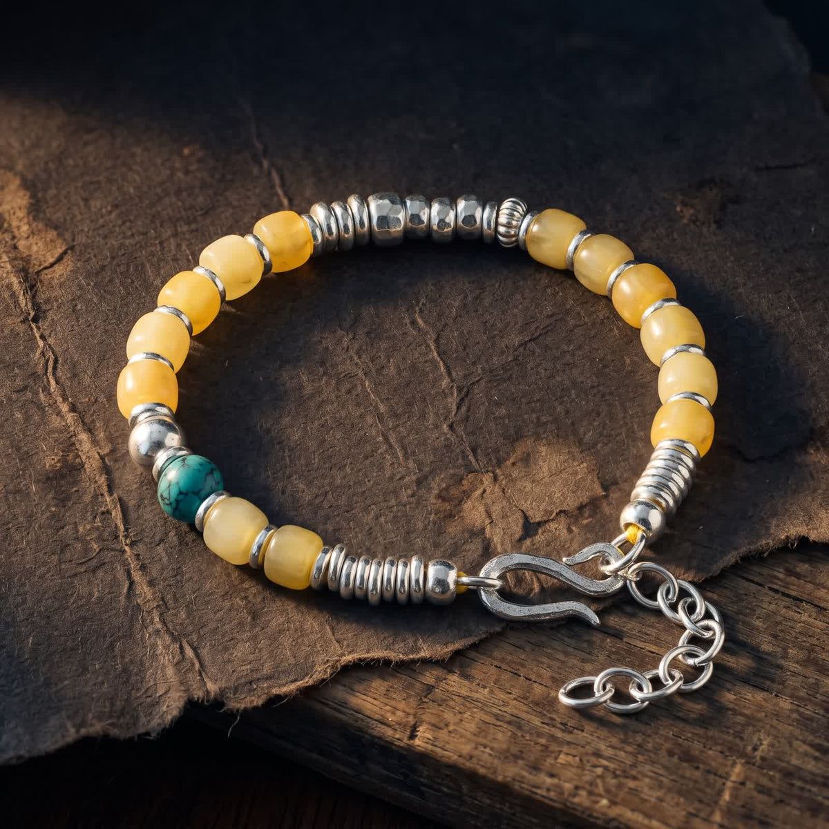 Honey-yellow bead bracelet with hammered sterling silver beads and a single turquoise bead on dark handmade paper over an old wooden board