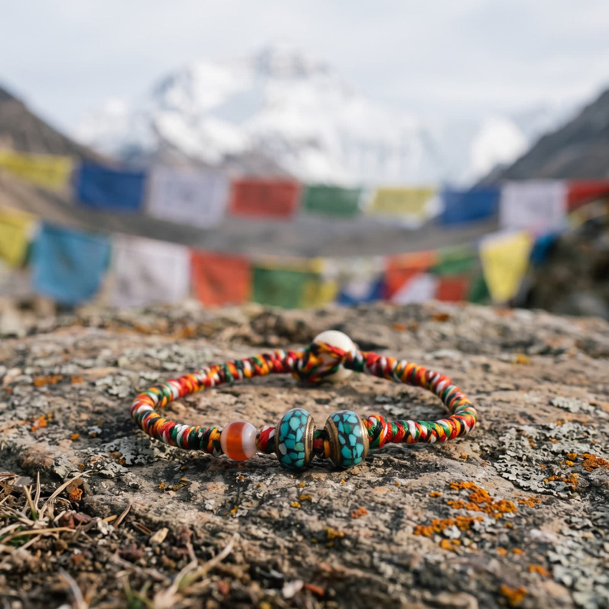 Five-color cord bracelet on a weathered rock, strings of prayer flags and a snow peak blurred behind