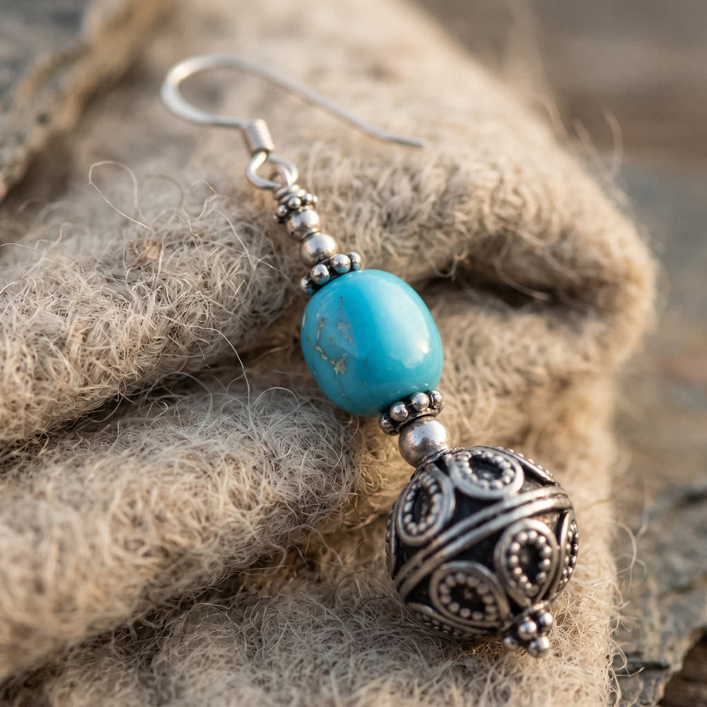 Close-up of the sky-blue turquoise nugget between granulated silvery bead caps on undyed wool