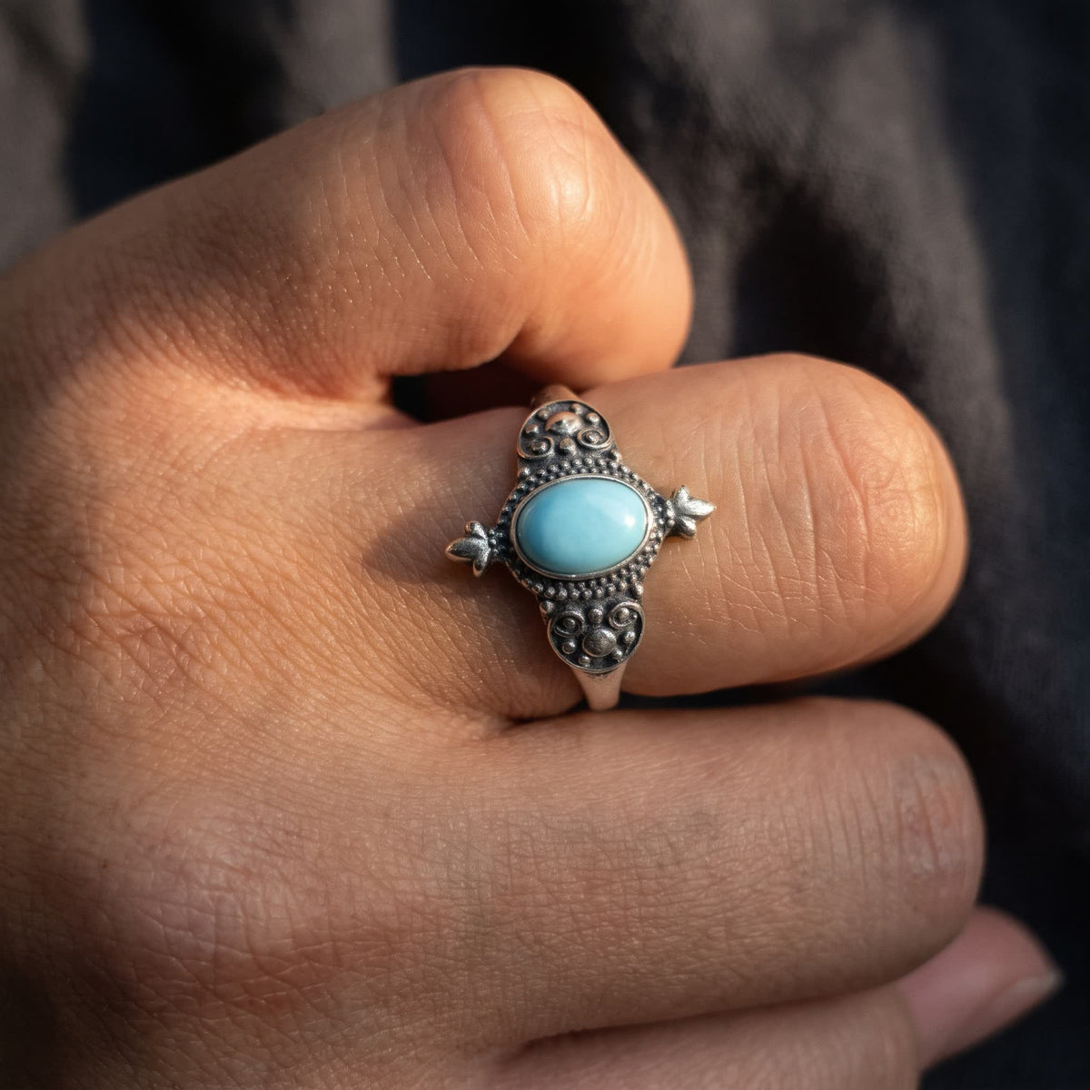 Oval turquoise ring with granulated scrollwork worn on a finger, the stone lying along the finger