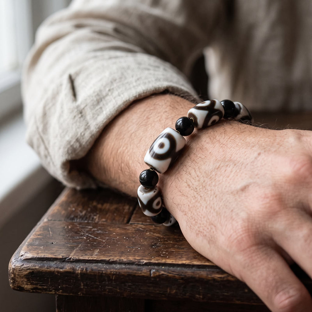 Agate dzi and black agate bead bracelet worn on a man's wrist, linen sleeve rolled back, resting on a wooden table