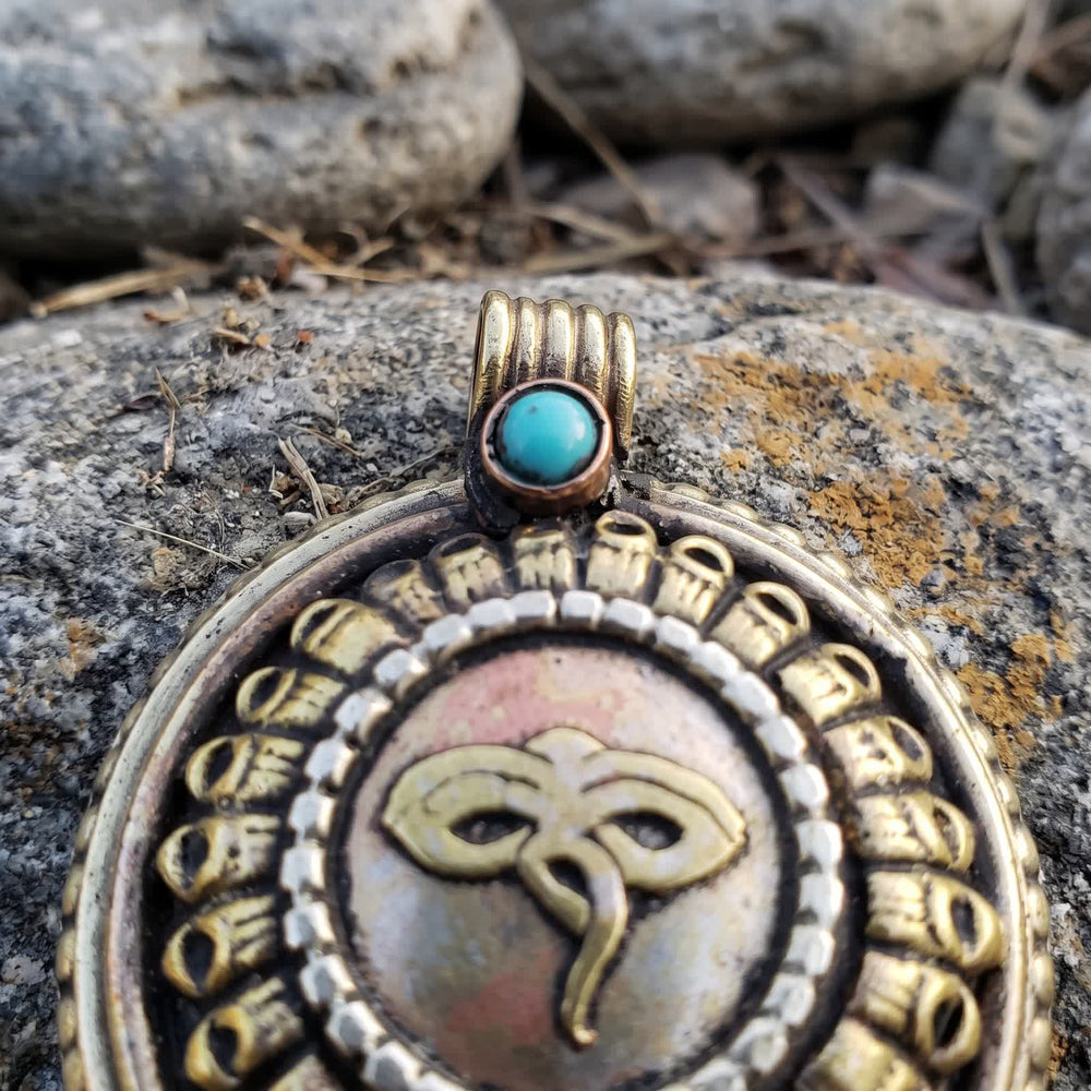 Close-up of the pendant's ridged bail with a small blue-green stone in a copper-red bezel above a ring of lotus petals