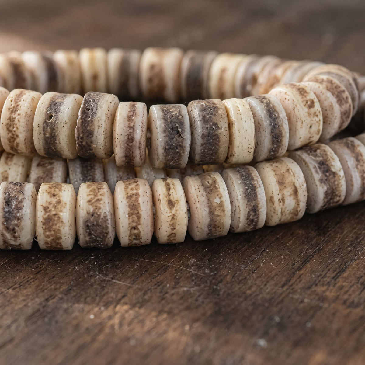 Close-up of ivory yak bone barrel beads with natural brown and grey banding on dark wood