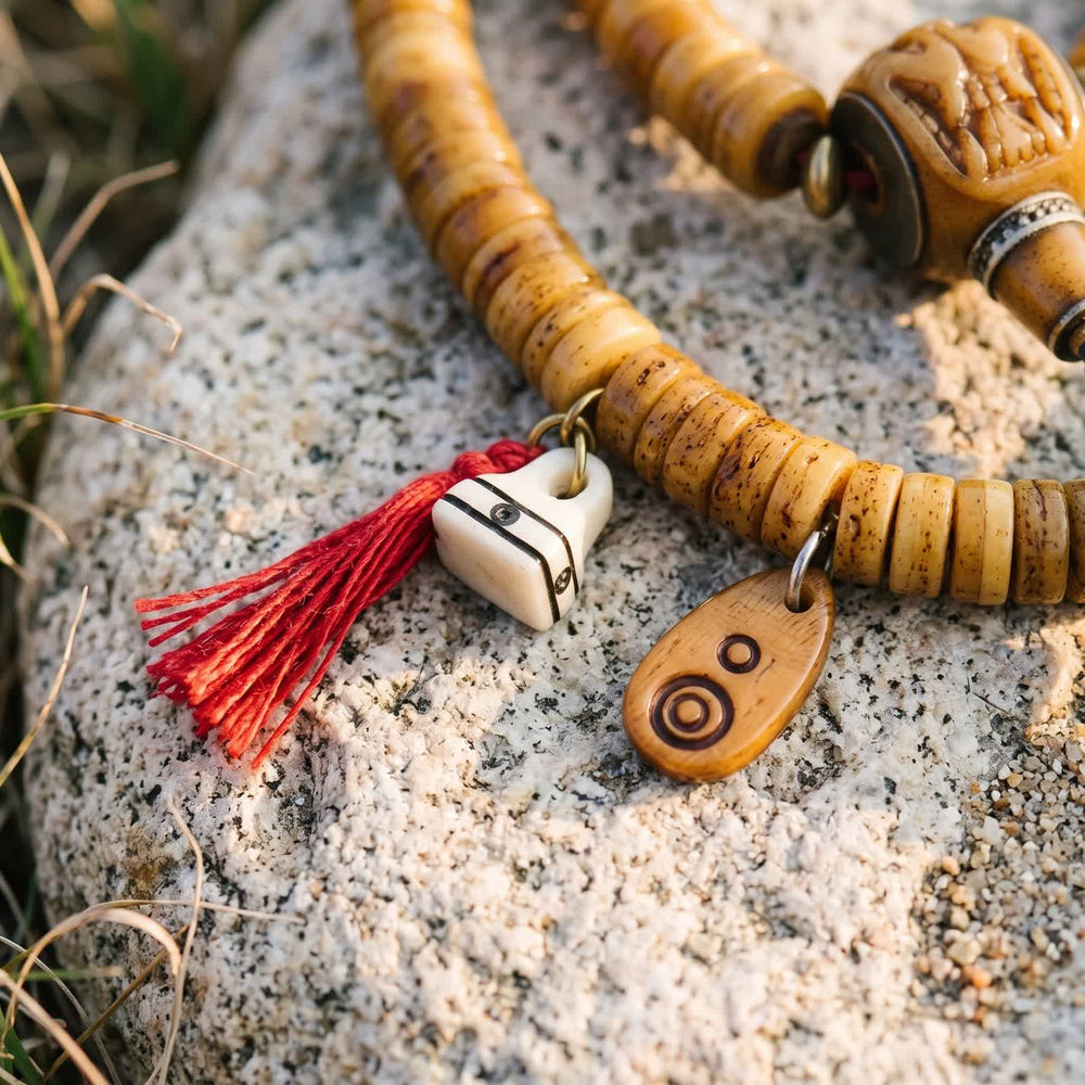 Small white bone charm with a red tassel and a bone tag carved with circles, hanging from honey yak bone disc beads