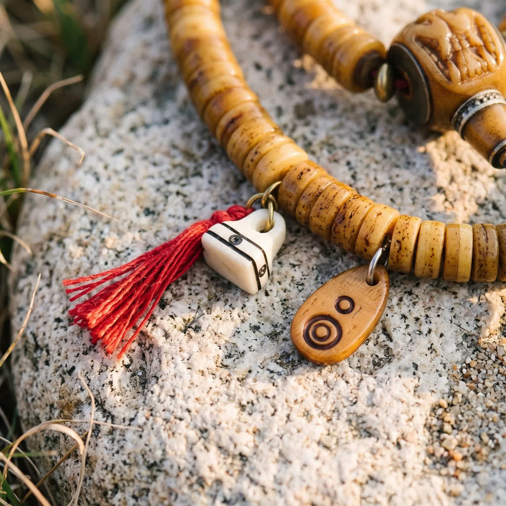 Small white bone charm with a red tassel and a bone tag carved with circles, hanging from honey yak bone disc beads