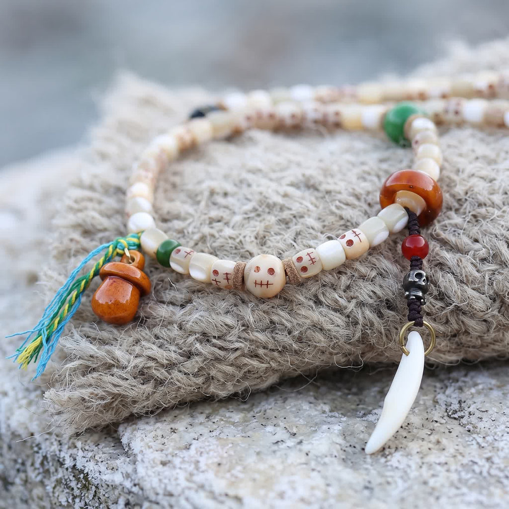 Orange carved gourd charm with a blue, yellow and green tassel, and a red bead, small metal skull bead and white tooth-shaped charm